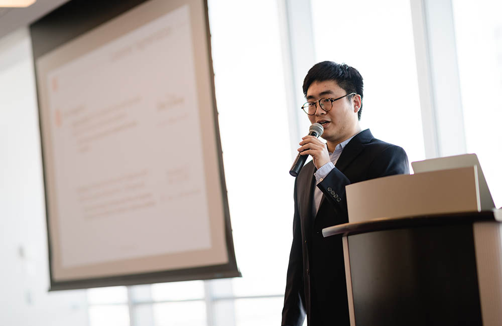 PECO co-founder, Peterson Jiang, stands at a podium and speaks into a microphone.