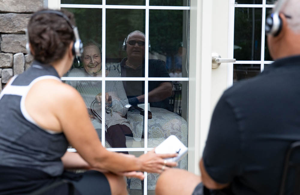 Visitors use Eversound headphones sets to visit at a safe distance with an assisted living resident.