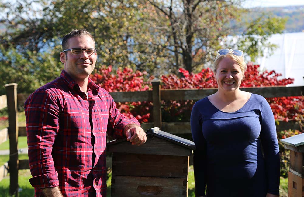 Nathan Oakes and Hailey Scofield of Combplex pose next to beehives at the. Wegmans Organic Farm.