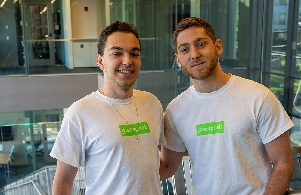 Photo of the founders of GlassGrab, Cornell students Gary Perelberg and Adam Schur. They are standing in a modern building wearing white shirts featuring the green GlassGrab logo.