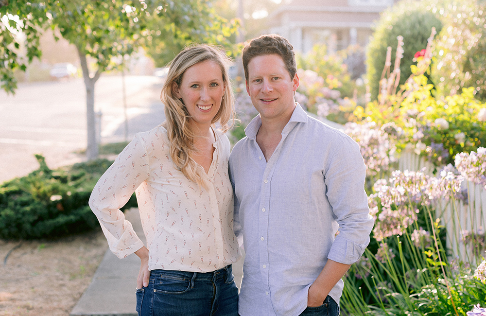 Photo of Sovi founders Julia and Alex Littauer standing in front of a floral background.