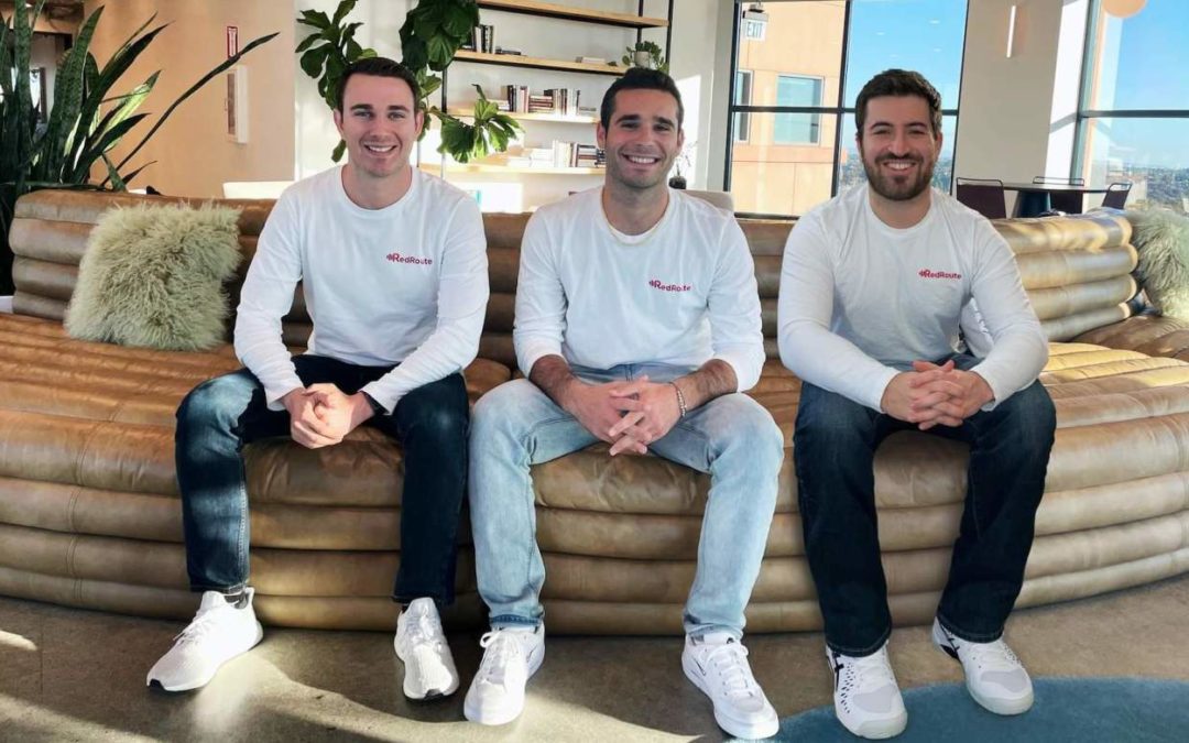 Three men wearing matching white t-shirts and jeans sit with their arms crossed