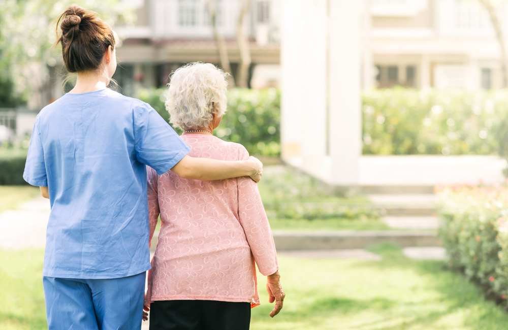 An elderly women stands outside with a female nurse.